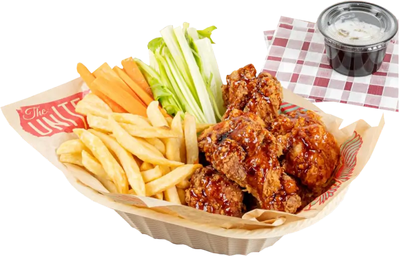 Food basket filled with crispy chicken wings glazed in sauce, french fries, celery, and carrot sticks, served on a custom-printed food basket liner with decorative text and patterns. Includes a dipping sauce in a plastic cup on the side