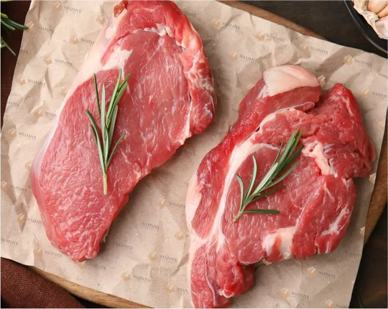 Two fresh cuts of raw steak garnished with rosemary, placed on custom butcher paper featuring the Wax Paper Global logo