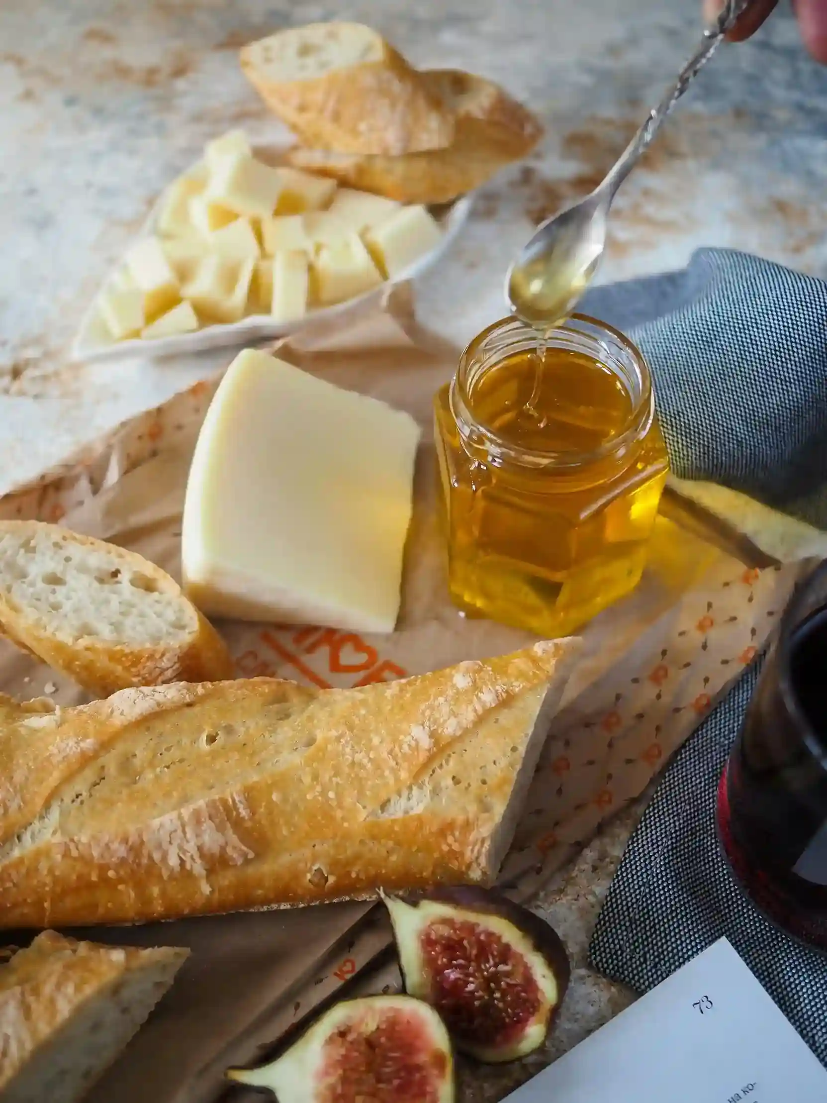 Fresh bread and blocks of cheese placed alongside a jar of golden honey and figs on custom-printed cheese paper