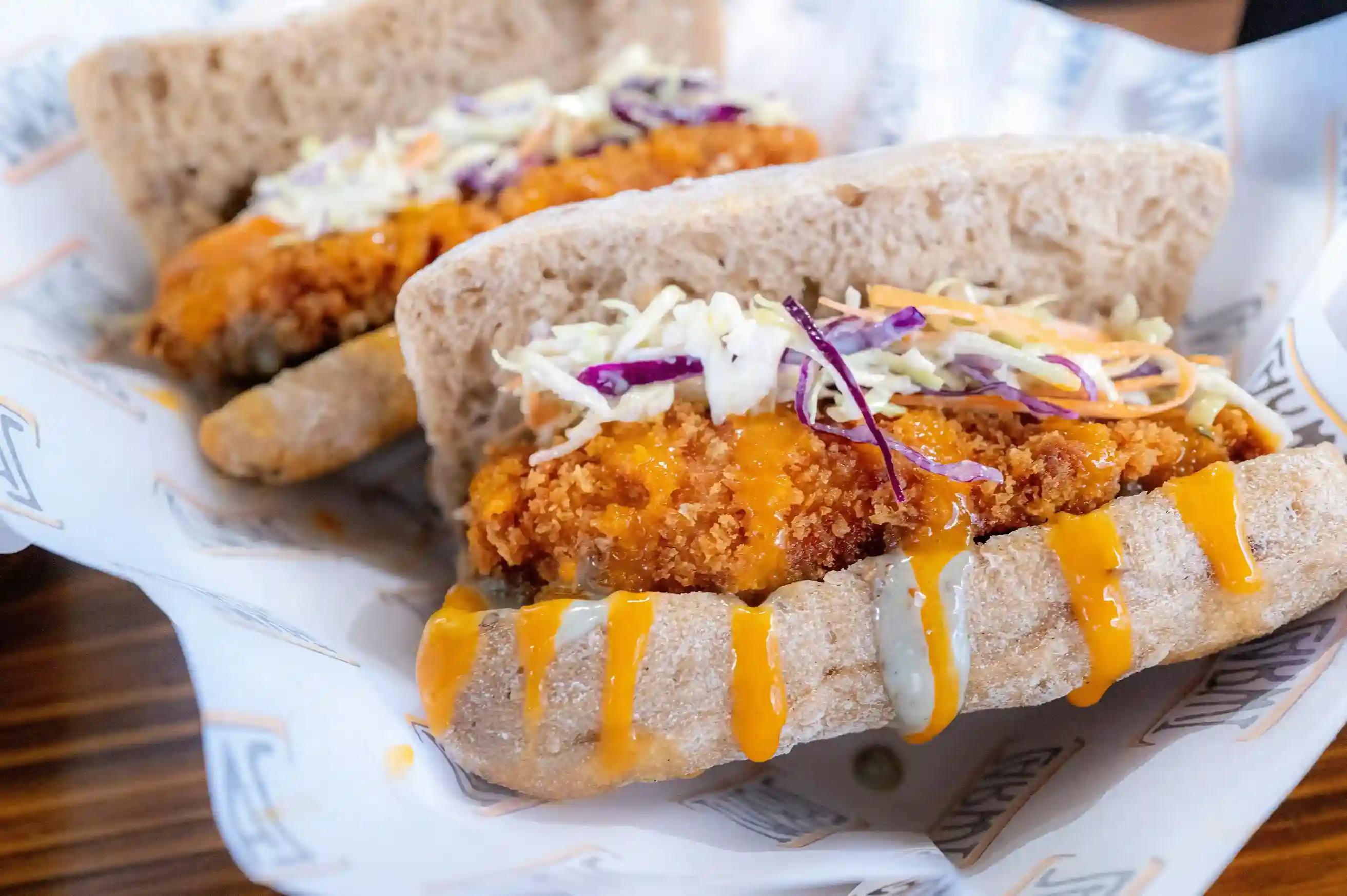 Crispy fried chicken sandwiches topped with coleslaw and drizzled with orange sauce, served on custom-printed deli paper