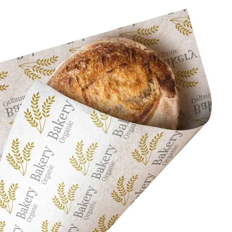 Freshly baked round loaf of bread wrapped in custom-printed deli paper featuring organic-themed wheat patterns and text