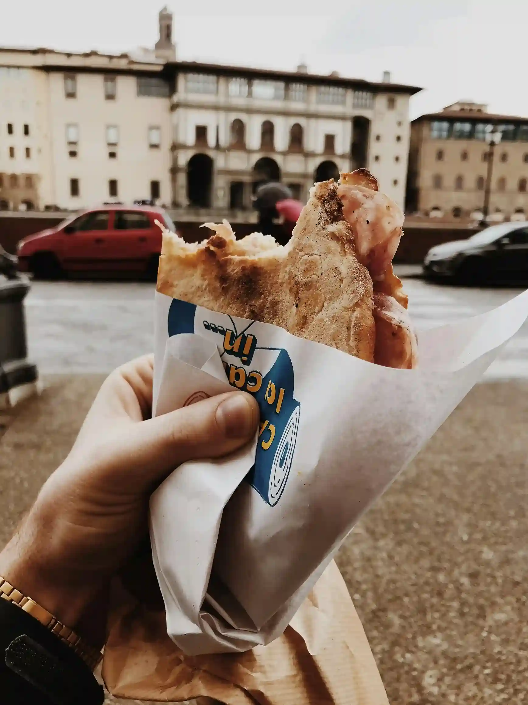 Street-style sandwich wrapped in branded custom food paper, held against an urban cityscape background