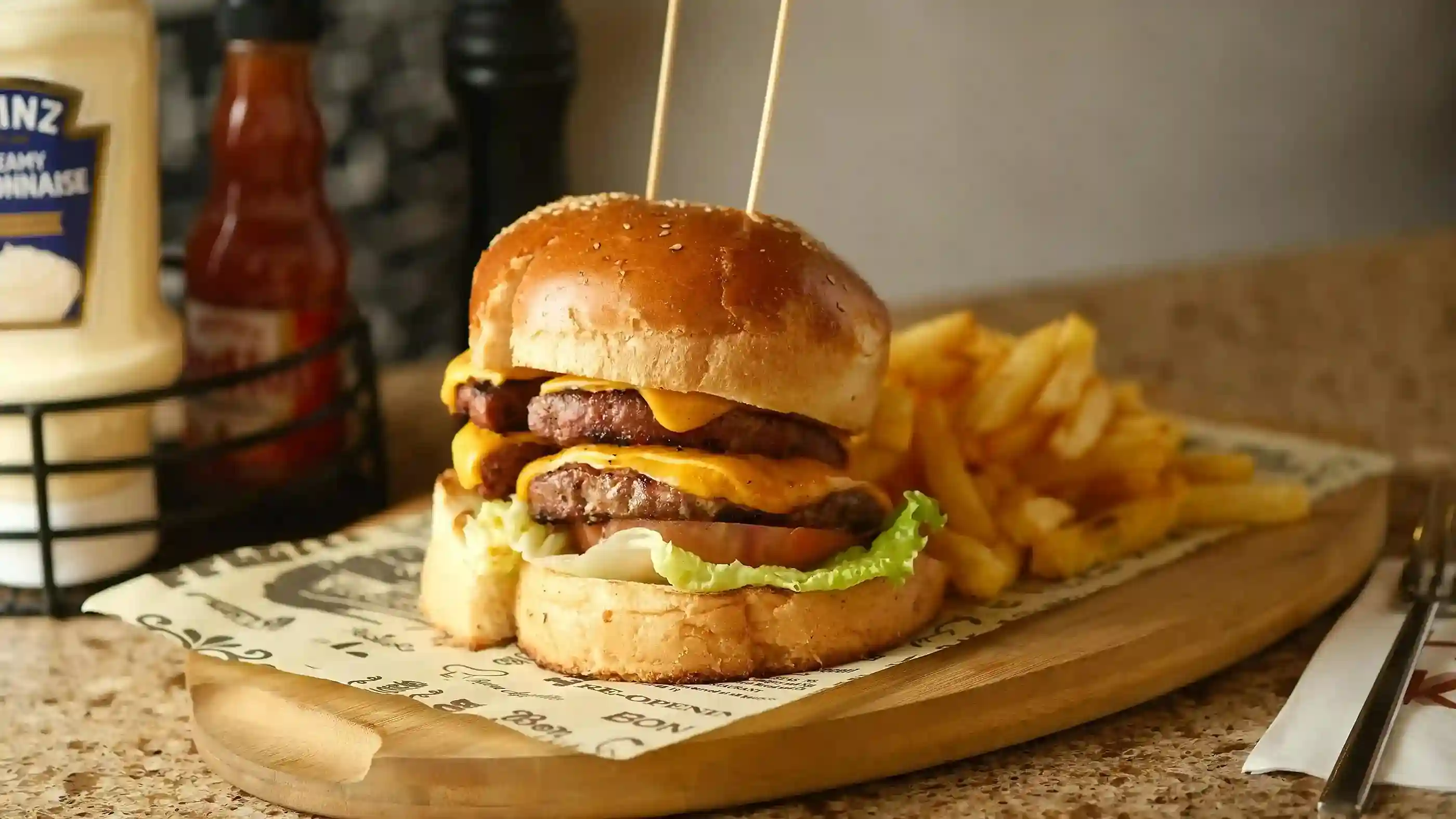 A double cheeseburger with fries served on a wooden board lined with custom-printed greaseproof paper