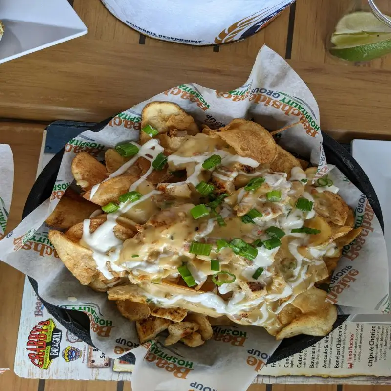 Loaded nachos with cheese sauce, sour cream, and chopped green onions served on a black skillet, lined with custom-branded hot paper for presentation