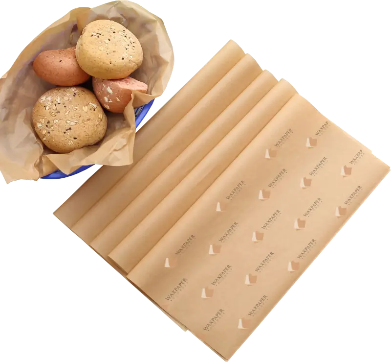 A bowl of fresh bread rolls placed next to folded sheets of custom-printed kraft paper featuring the Wax Paper Global logo