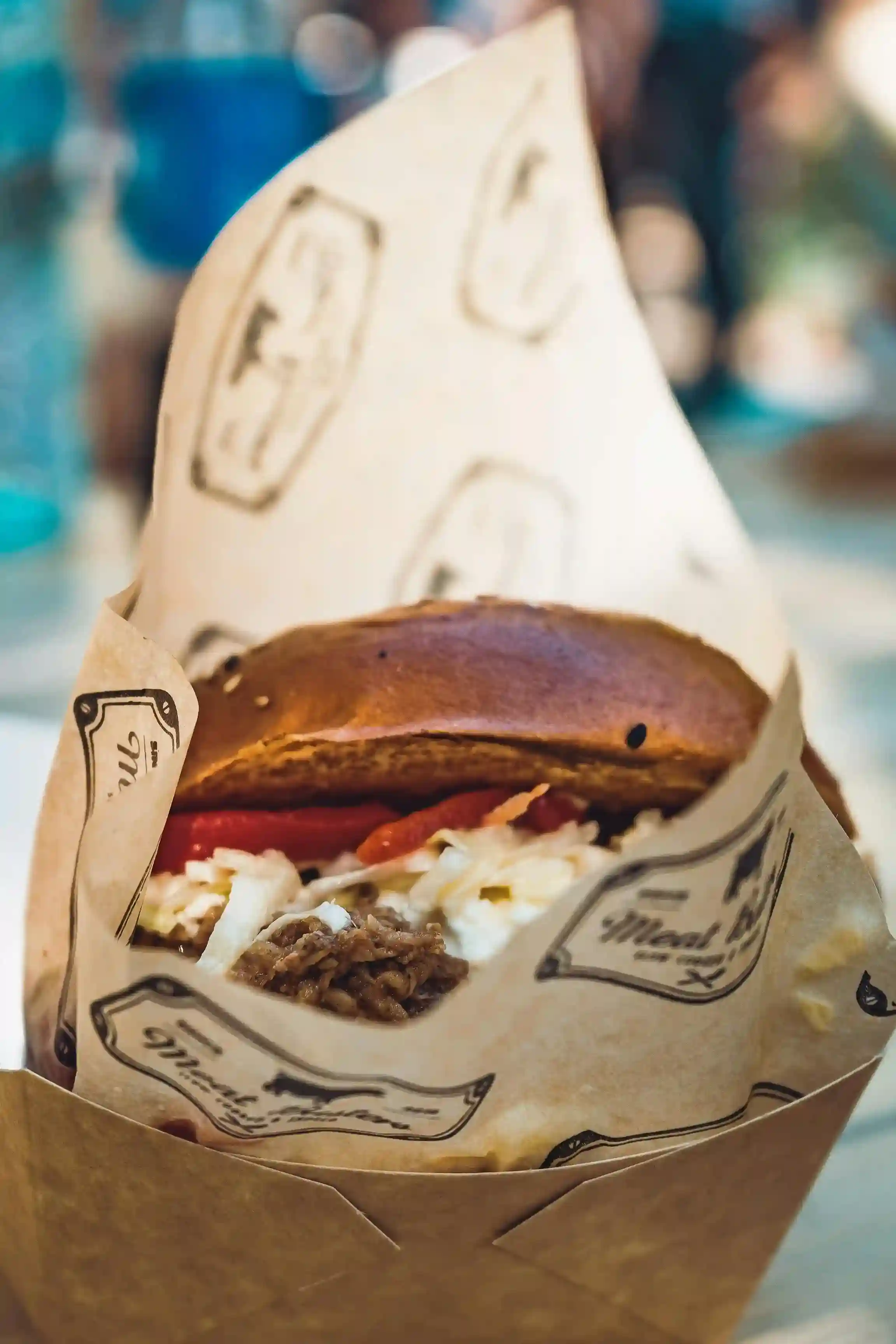 Close-up of a gourmet burger wrapped in custom-printed kraft paper with a rustic logo design, served in a takeaway box