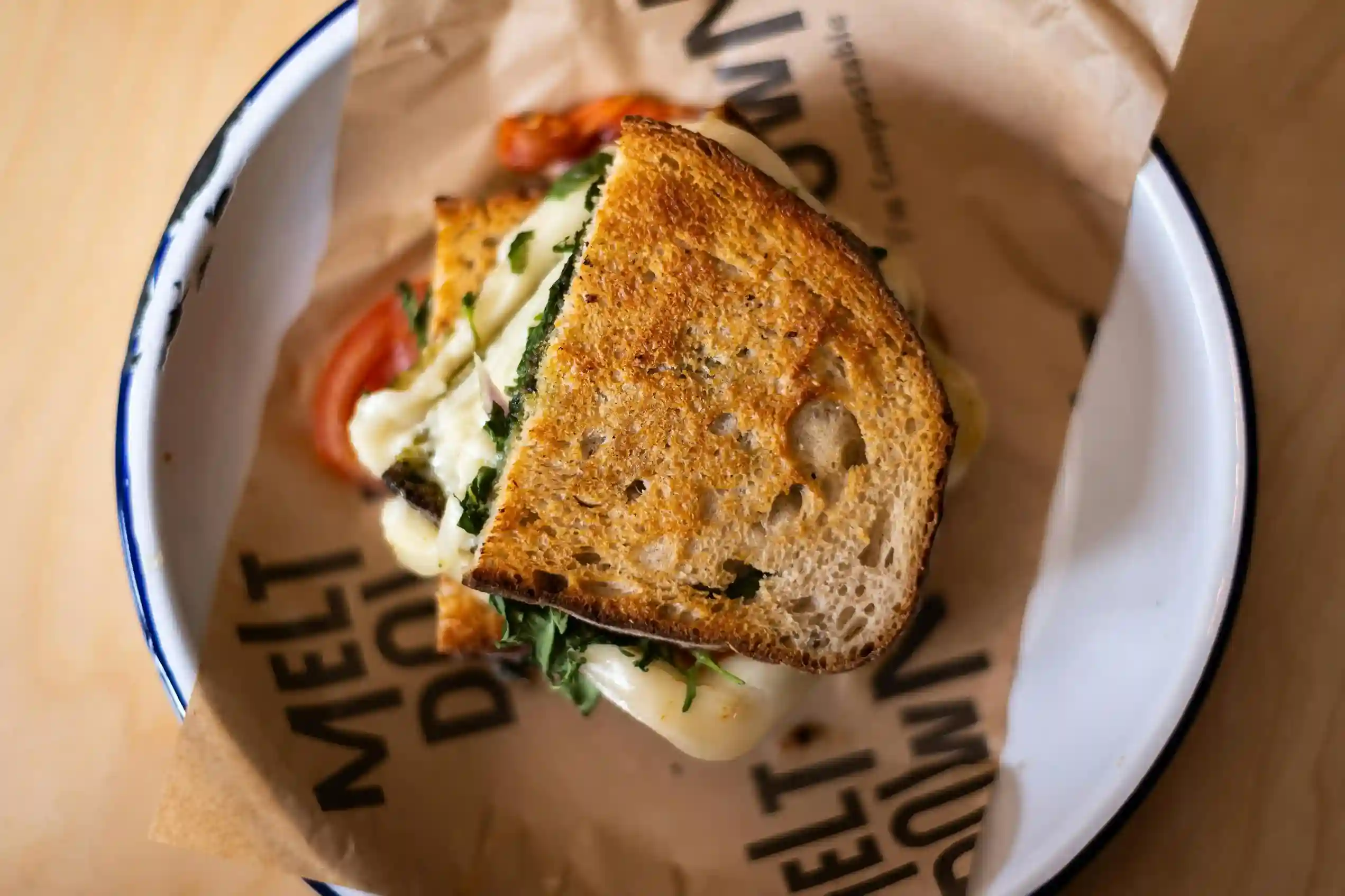 A grilled cheese sandwich served on a plate lined with custom-printed kraft paper featuring bold text design