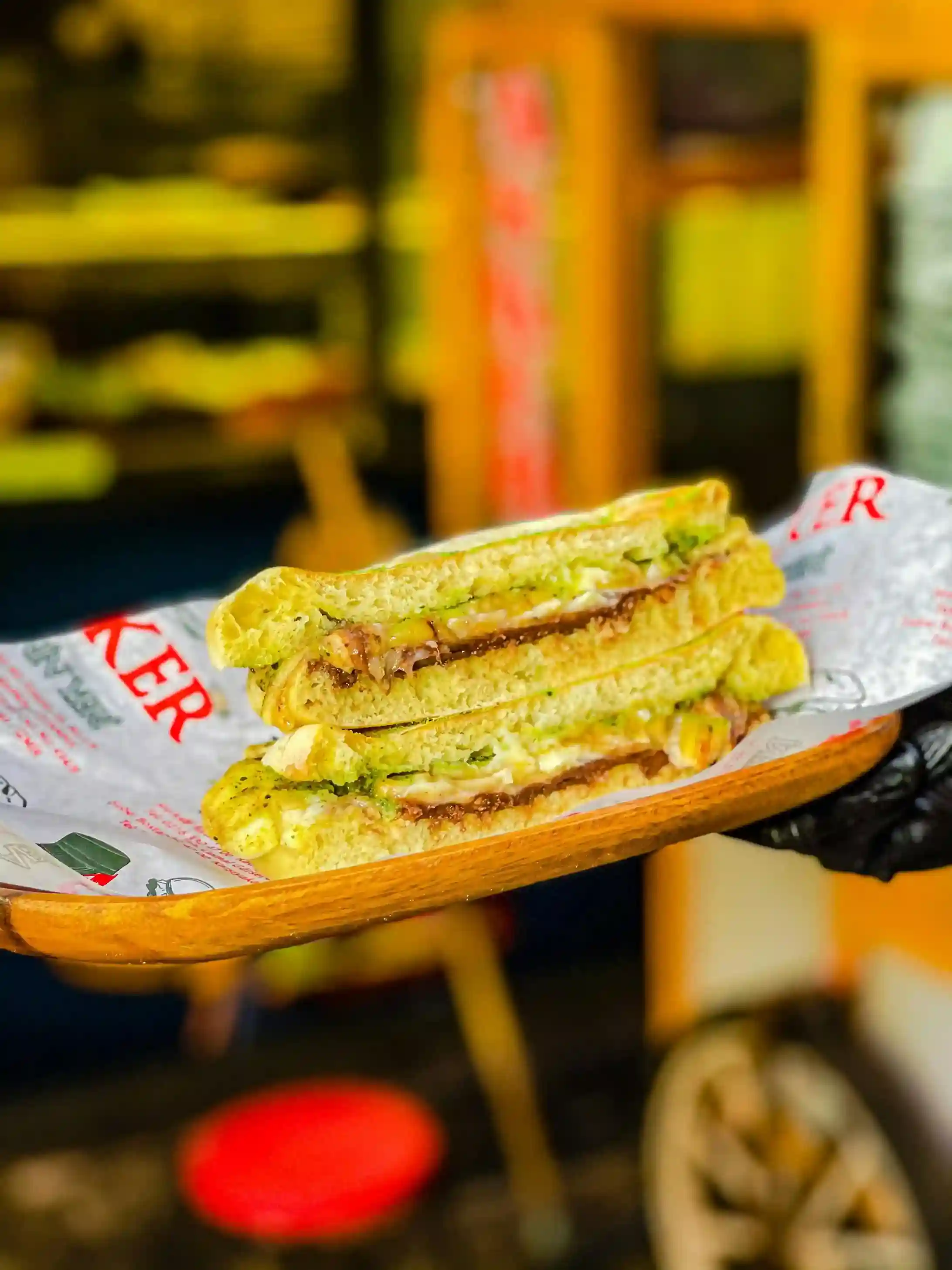 A close-up of stacked sandwiches served on a wooden platter, lined with custom-printed sandwich paper featuring vibrant text and illustrations