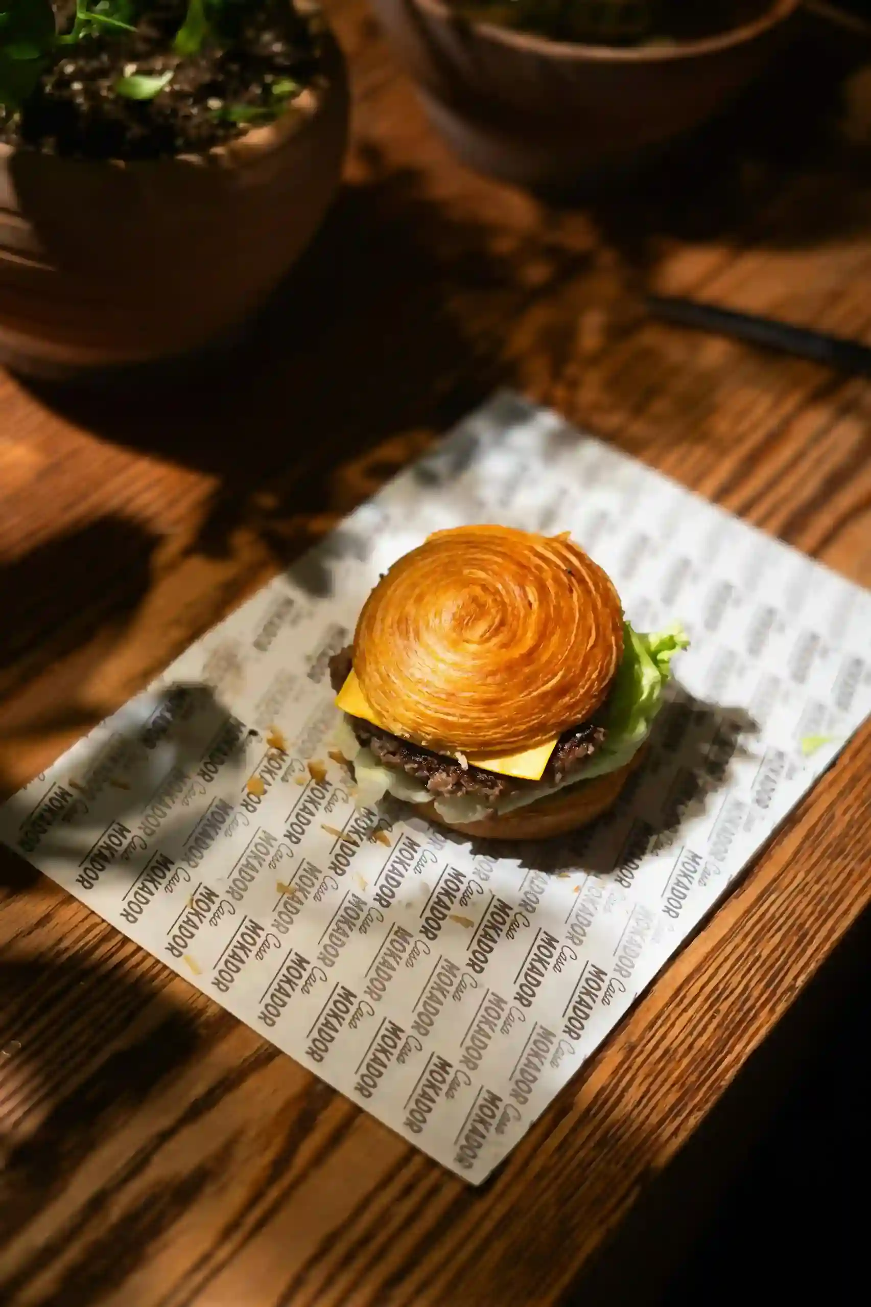 Burger with a brioche bun, served on custom printed wax paper in a cozy cafe setting