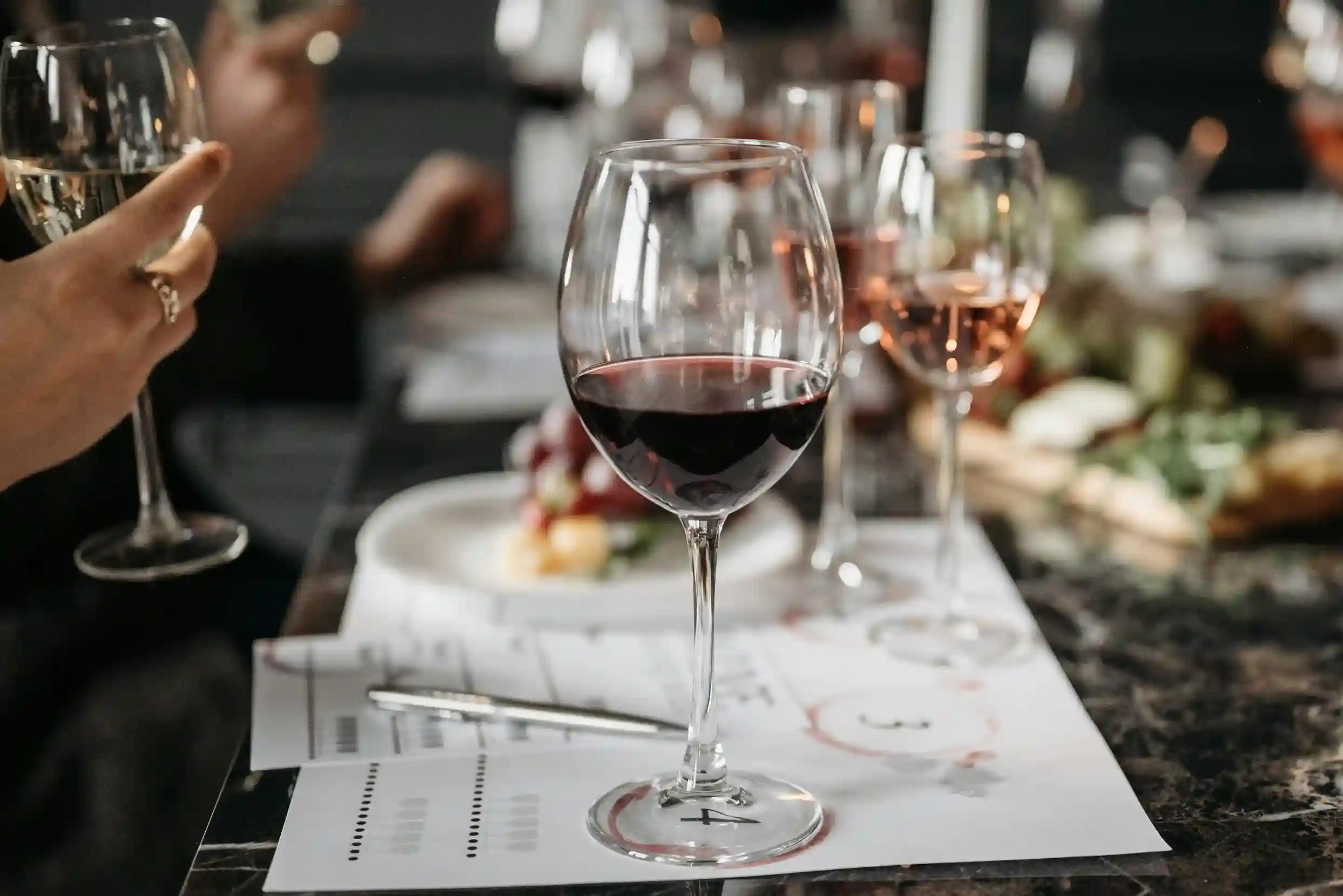 Glass of wine on a table in a restaurant setting, with food served on custom printed wax paper in the background