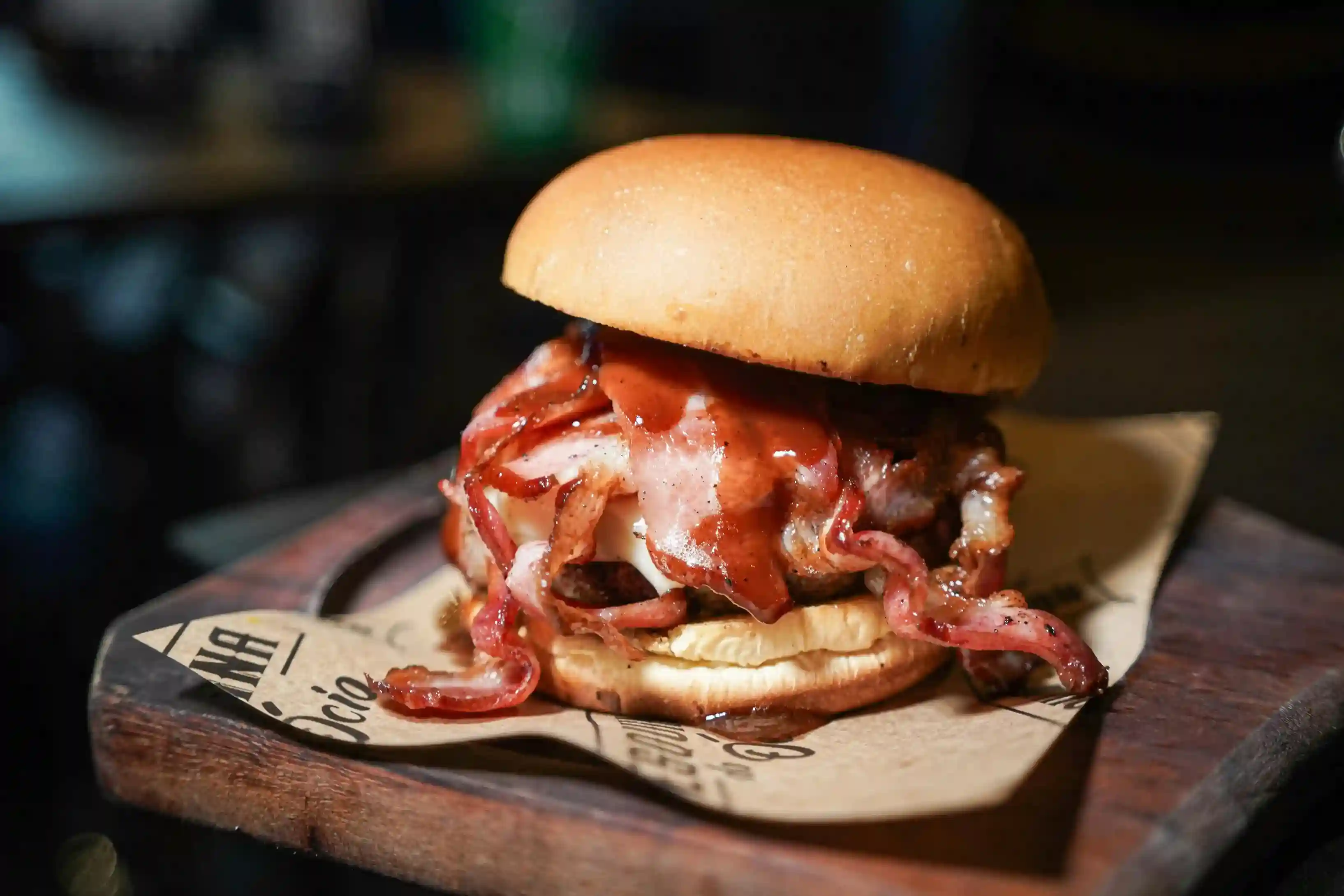 Juicy bacon cheeseburger served on custom-printed kraft paper, enhancing its rustic presentation on a wooden tray