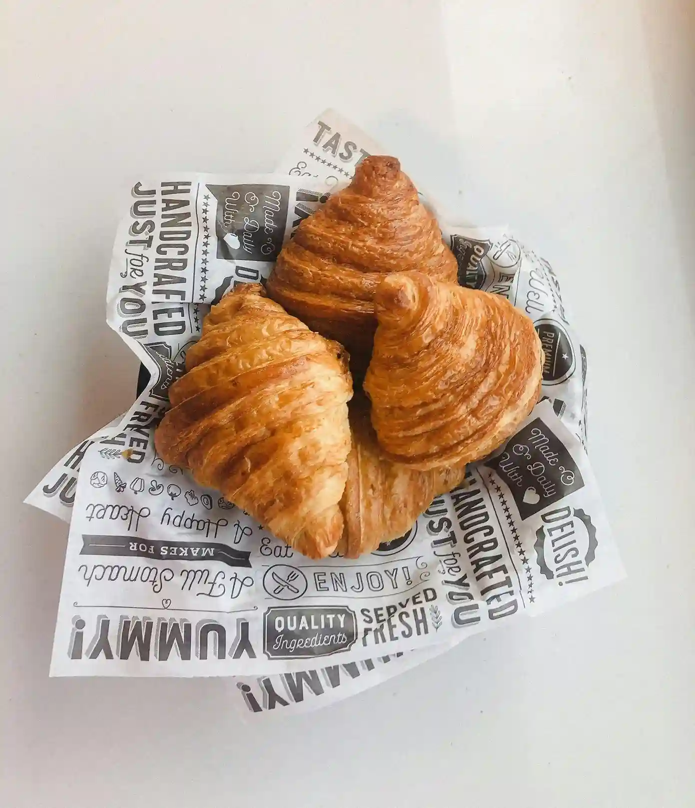 Three freshly baked croissants placed on custom-printed deli paper featuring stylish text and designs