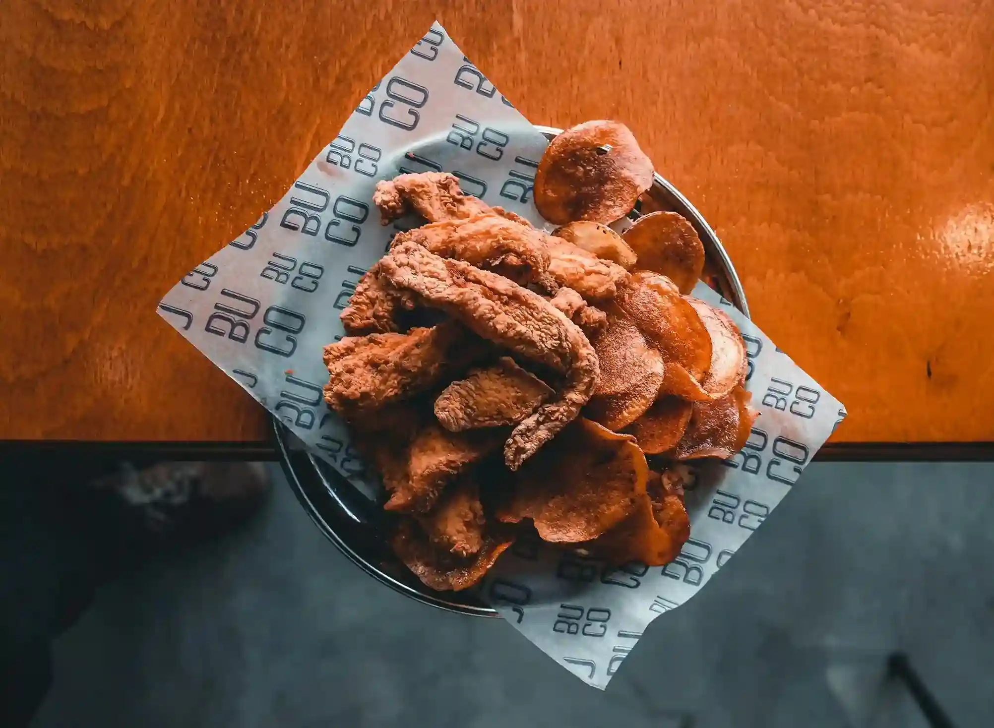 Crispy fried chicken tenders and seasoned potato chips served on a custom-printed hot paper liner in a black pan on a wooden table