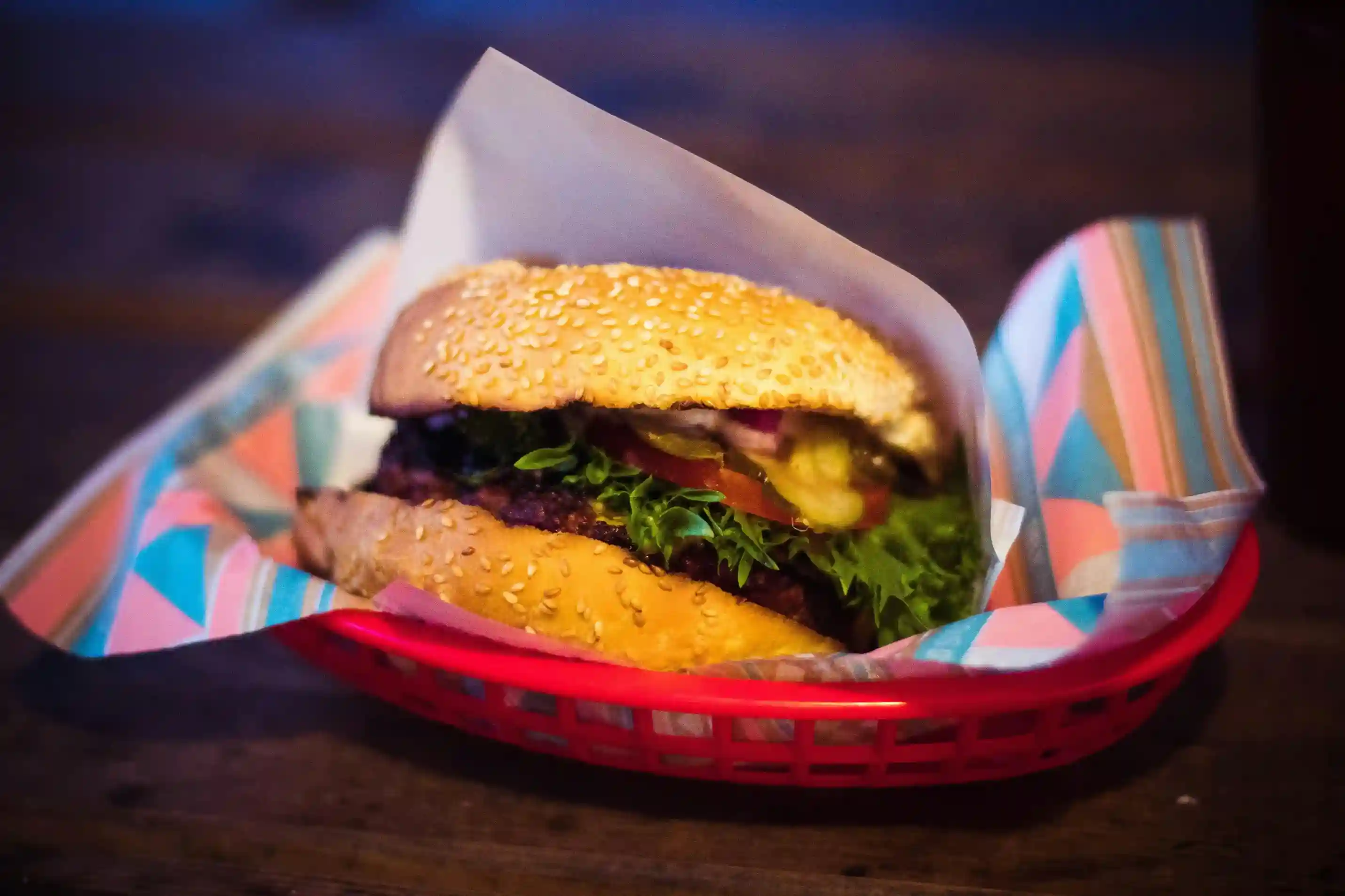 Juicy sesame seed burger with fresh lettuce, tomatoes, and pickles served in a red basket lined with colorful custom-printed food basket liner for vibrant presentation and prevent leaks